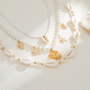 Detalle de cadena corporal de perlas bohemias con dijes de estrella de mar sobre arena