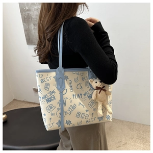 Detail of a large cream tote bag with blue graffiti and a cute knitted bear charm