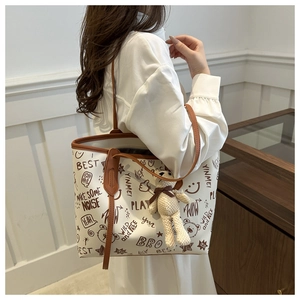 Detail of cream tote bag with brown graffiti patterns and leather straps on model