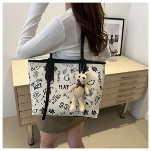 Detail of white tote bag with black graffiti prints and a cute knitted bear pendant