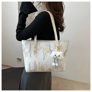 Detail of white tote bag featuring colorful embroidery and a plush cloud charm accessory