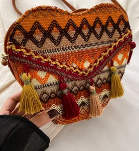 Detalle de bolso étnico trenzado en forma de corazón con borlas de colores y correa de cuero