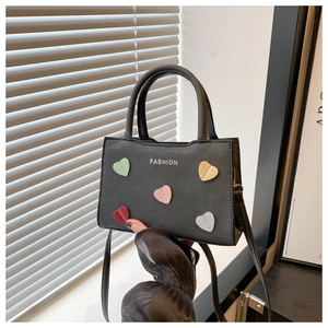 Close-up of black PU leather handbag with colorful heart patches and fashion text