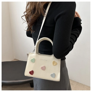 Detail view of cream white crossbody bag with colorful heart patches and silver lettering