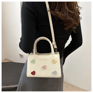 Rear view of a chic cream handbag with colorful heart patches and adjustable shoulder strap