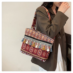 Ethnic embroidered tote bag with colorful tassels worn by a model in a brown blazer