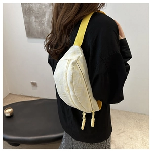 Détail d'un sac bandoulière tissé beige avec sangle jaune porté par un mannequin