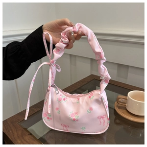 Pink floral nylon bag with pleated handle and bow details shown in a lifestyle setting