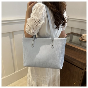 Detail of light blue pleated tote bag with silver rivets worn by a model in white