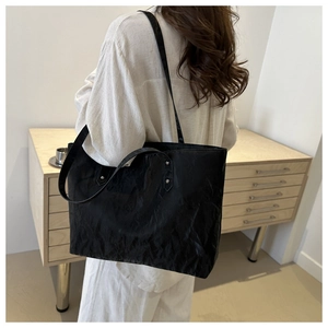 Macro detail of black pleated tote bag showing the matte textured finish and shoulder straps