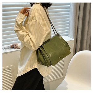 Olive green chain shoulder bag in glossy leather worn by a model in a casual urban style