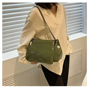 Deep green glossy leather crossbody bag with chain strap worn by a model in casual style
