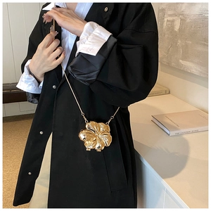 Detail of a 3D gold floral metal clutch with snake chain strap worn over a black blazer