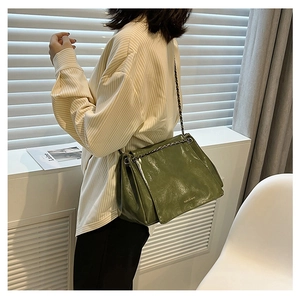 Macro view of dark green patent leather shoulder bag with glossy texture and chain strap