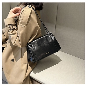 Detail of black faux leather crossbody bag with gold lettering and metal chain strap
