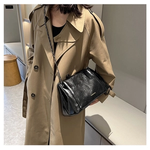 Detail of black glossy wrinkled crossbody bag with chain strap on khaki trench coat