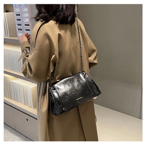 Detail of a black glossy crossbody bag with gold chain strap on a khaki trench coat