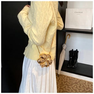 Detail of a metallic gold flower crossbody bag with chain strap on a model outfit