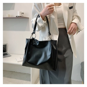 Close-up of black leather tote bag featuring a silver metal ring and slender shoulder strap