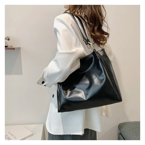 Detail of a large black tote bag in glossy leather worn by a model in casual attire