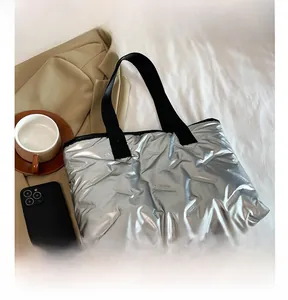Silver metallic down tote bag detail with quilted pattern and black handles on bed