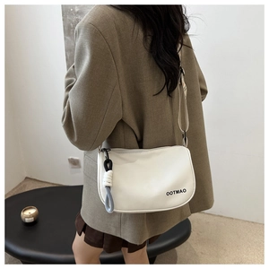 Détail d'un sac bandoulière blanc avec logo et pendentif décoratif en corde nouée