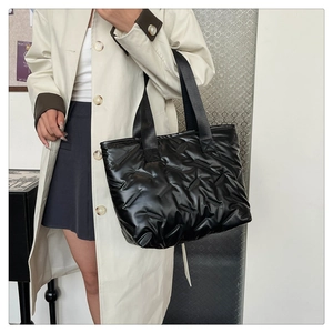Quilted black puffer tote bag with glossy finish shown on model in modern minimalist setting