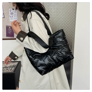 Close-up of black glossy quilted puffer tote bag with ribbon details and wide strap