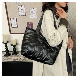 Close-up of black quilted puffer tote bag featuring a glossy texture and wide strap