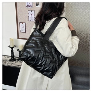 Detail of glossy black quilted tote bag with wide strap and padded geometric texture