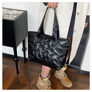 Detail of black glossy quilted tote bag with wide padded woven texture for winter