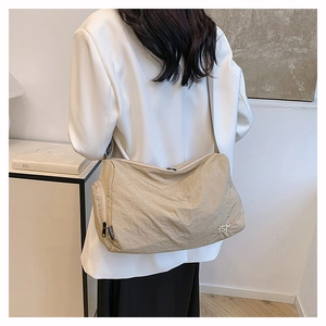 Detail of a khaki nylon crossbody bag showing the wrinkled texture and side zipper pocket