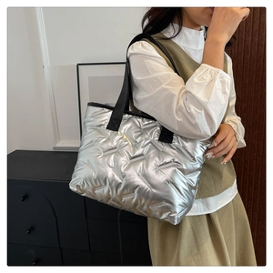 Detailed shot of silver quilted tote bag with black strap worn by a model in interior setting