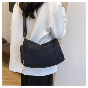 Detail of black nylon crossbody bag with adjustable strap and fashion label on zipper
