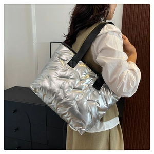 Detail of silver quilted tote bag with black straps in a minimalist lifestyle setting