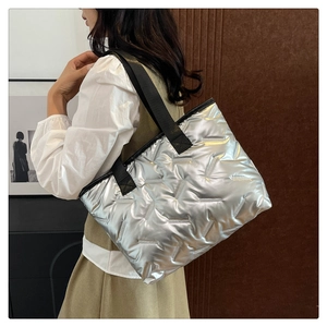 Detail of silver quilted tote bag with metallic finish and black straps on a female model