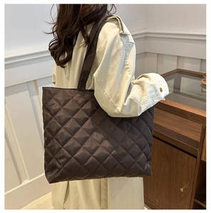 Detail view of dark brown quilted tote bag on shoulder showing texture and capacity