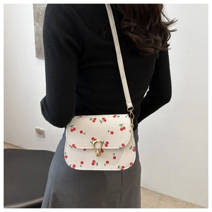 Detail view of white crossbody bag with red cherry prints and golden metal clasp closure