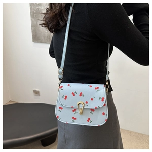 Close-up of a blue crossbody bag with cherry prints and a golden buckle on a model