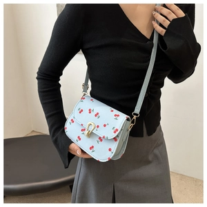 Detail shot of light blue cherry print crossbody bag with gold horseshoe buckle closure