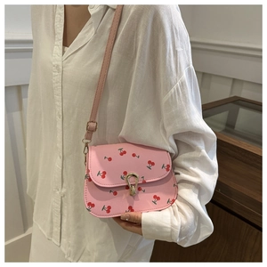 Detail of pink crossbody bag with red cherry prints and golden lock closure
