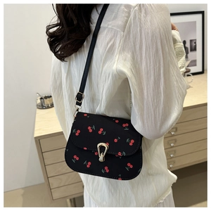 Detail of crossbody bag with red cherry print and golden teardrop clasp on a model