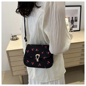 Detail of black saddle bag with red cherry pattern and gold metal buckle on shoulder