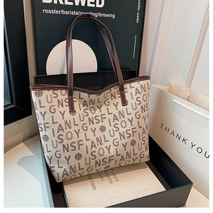 Detail of canvas tote bag with letter print and brown leather handles in gift box