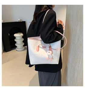 Detail showing white embossed tote bag with pink trim and a fluffy keychain on a model