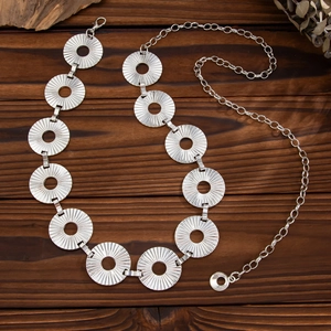 Silver punk metal body chain with hollow sunburst textured rings on dark wood background