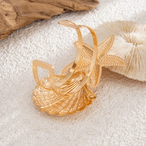 Close-up of golden starfish and seashell arm cuff on beach sand with coral