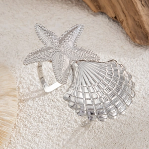 Silver ocean starfish shell napkin rings on beach sand with corals for seaside decor