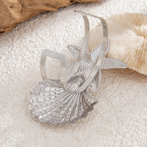 Detail view of silver seashell and starfish cuff bracelet on a sandy beach setting