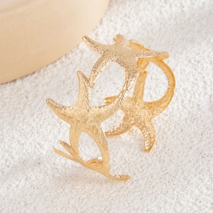 Close-up of golden starfish open cuff with hammered metal texture on sand-like background